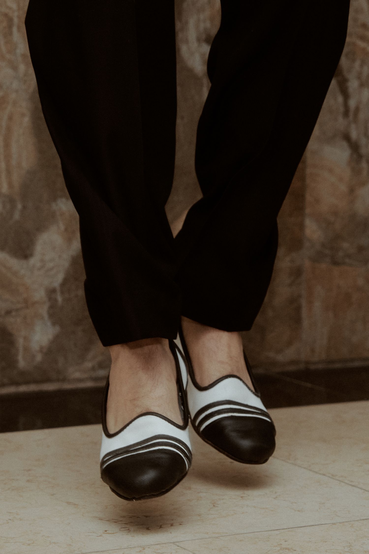 Close-up of black and white formal shoes against textured floor.