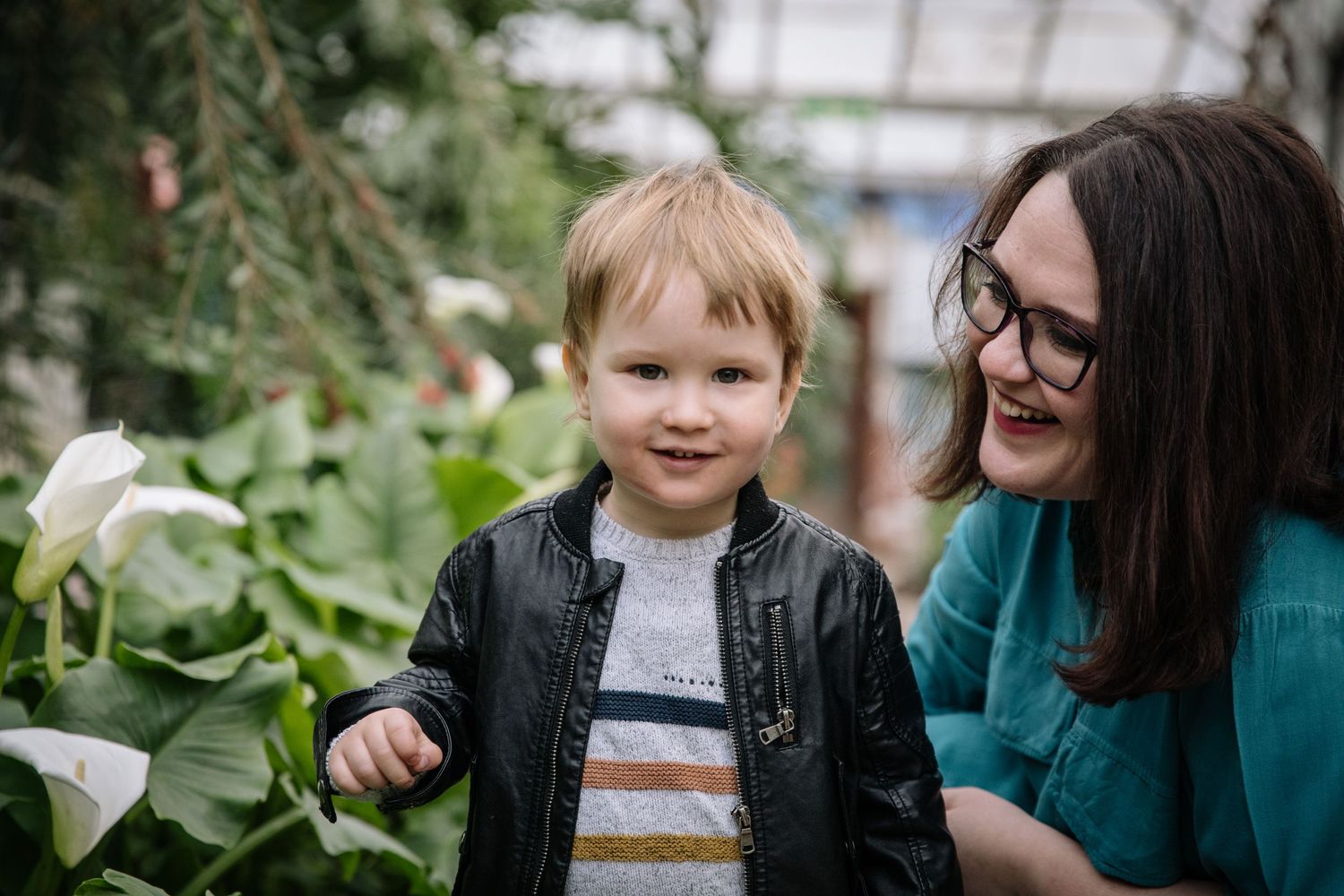 Mother and child share joyful moment among greenhouse plants and flowers.