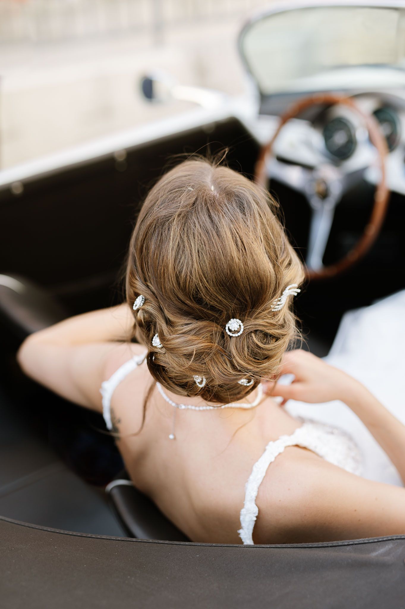 An elegant bridal hairstyle with pearl pins seen from behind in a vintage convertible car.