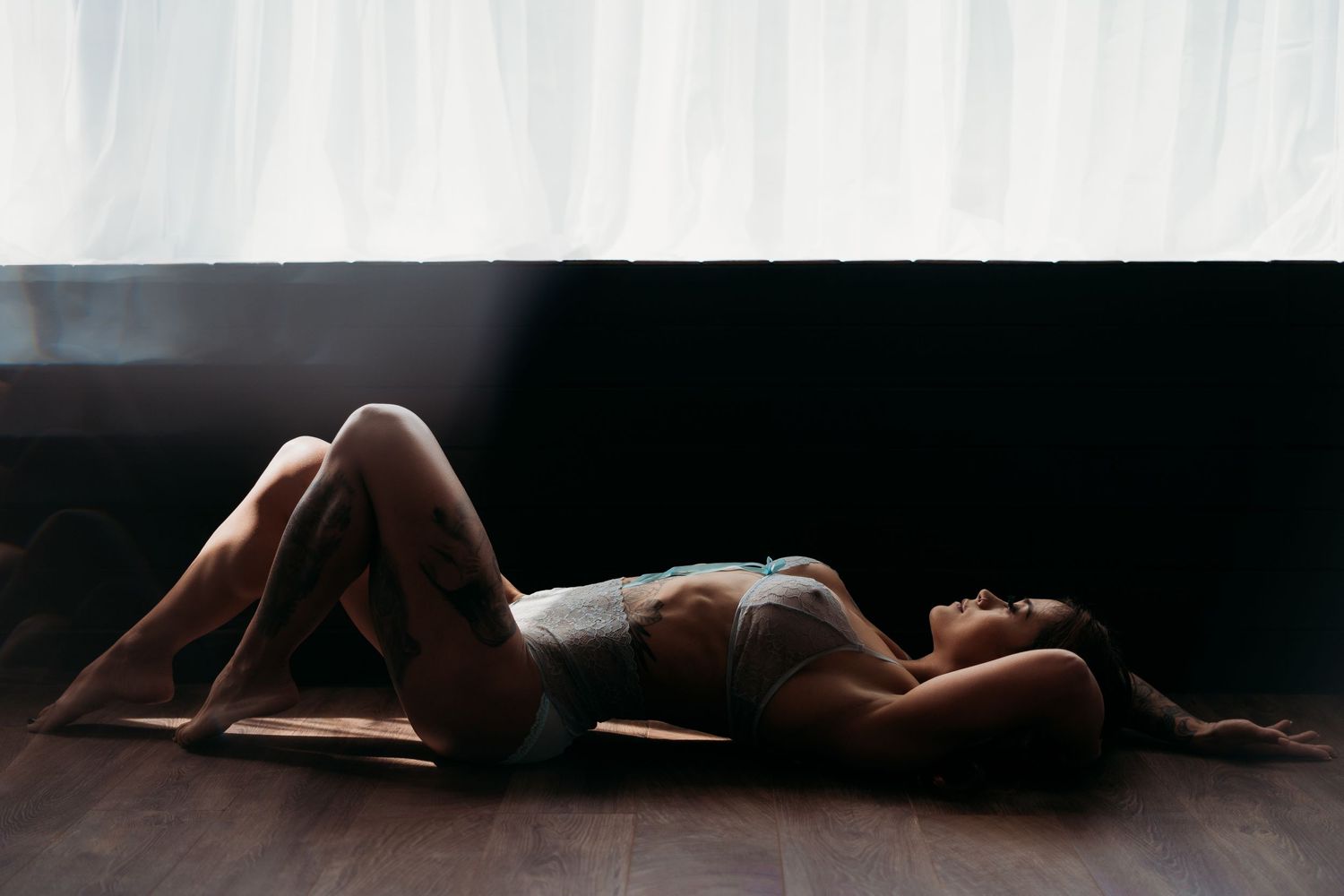 Artistic silhouette boudoir photo with dramatic lighting on dark wooden floor.