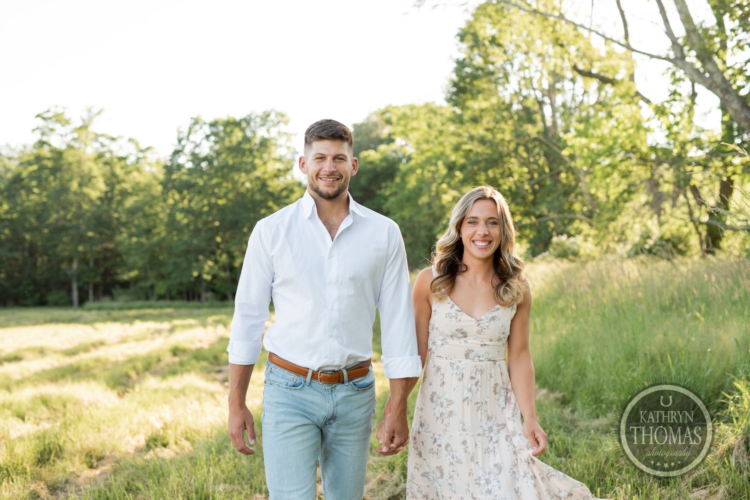 A couple stands together in a sunny meadow wearing coordinating casual outfits.