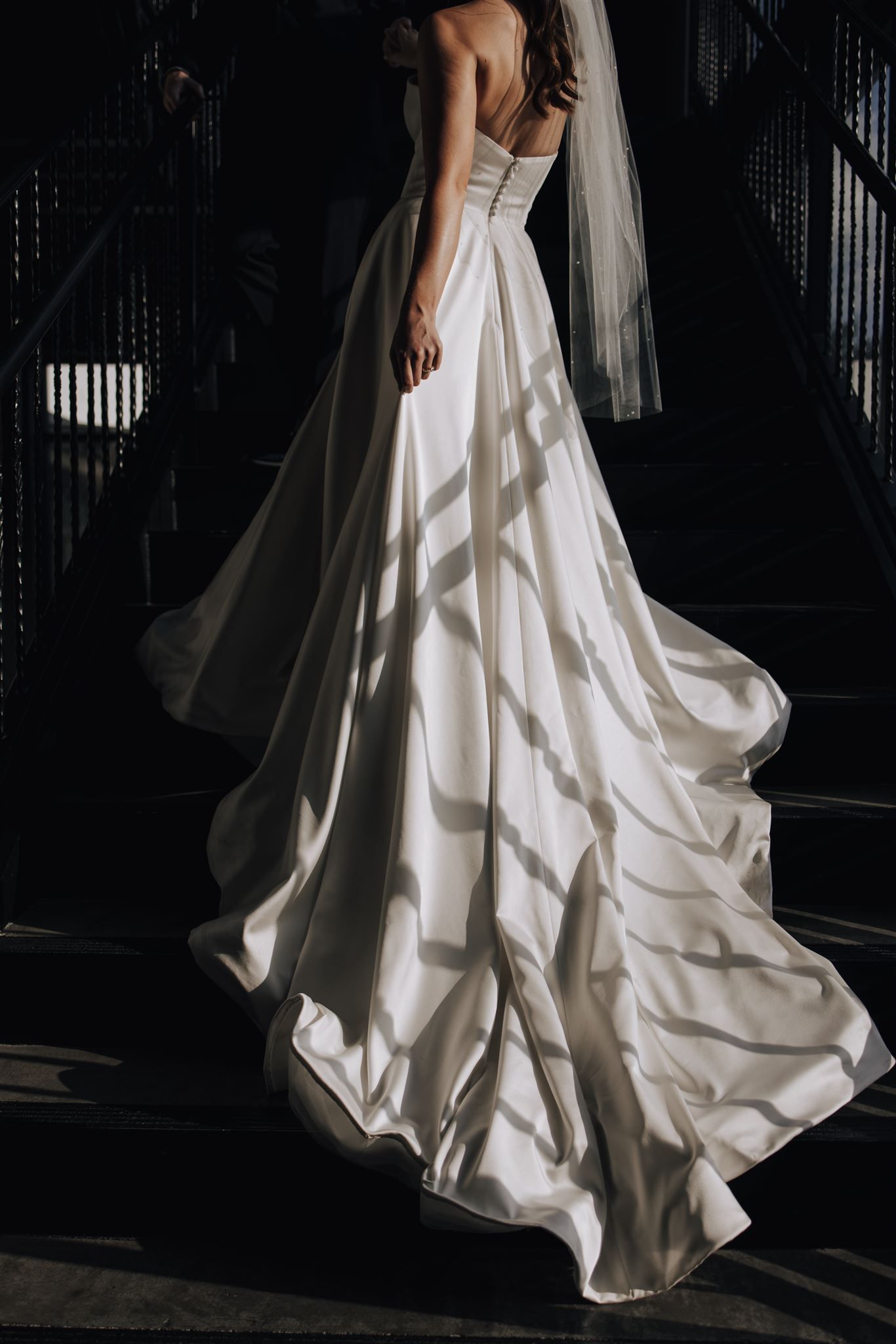 A flowing white wedding gown with dramatic train photographed in moody lighting.