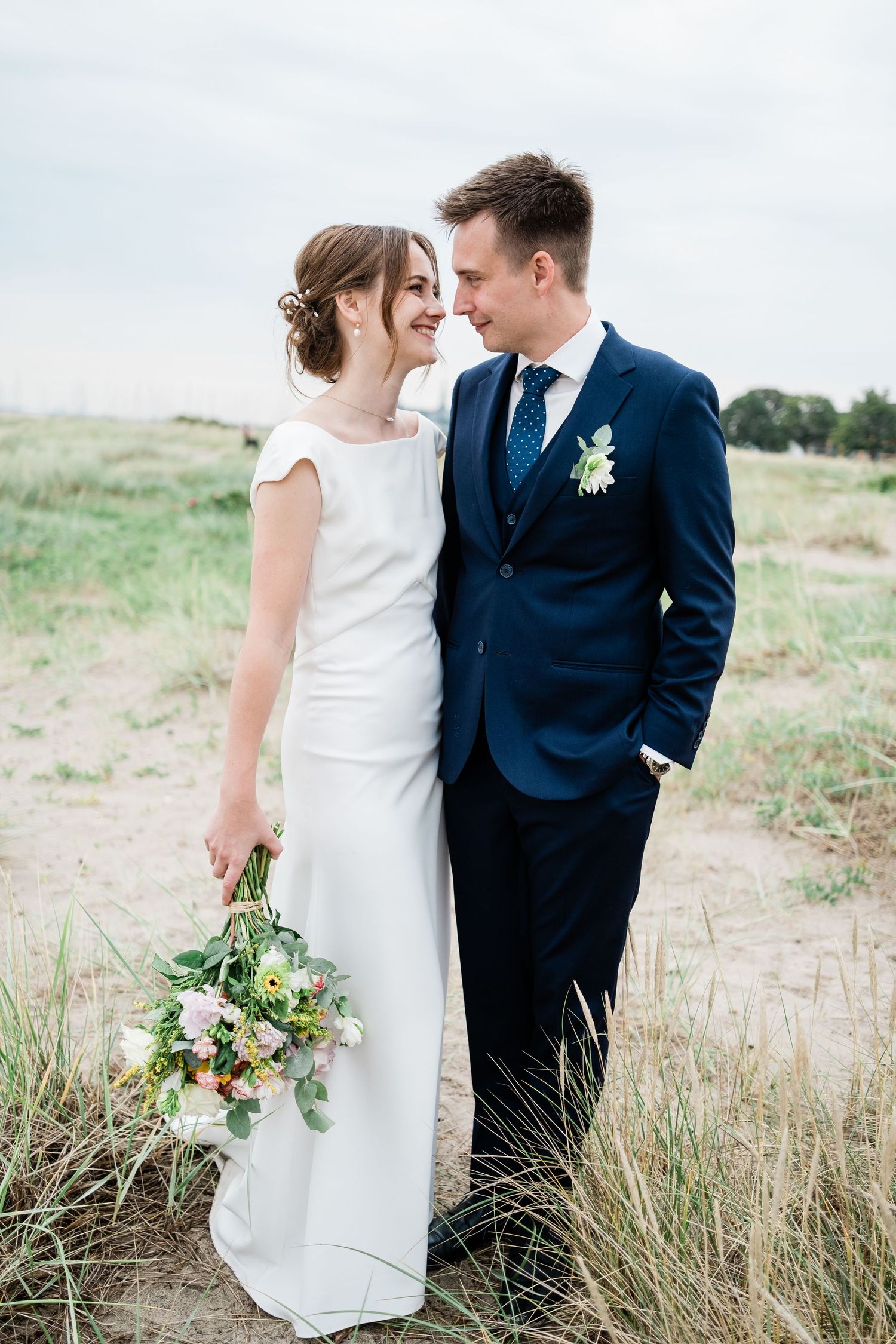 Elegant wedding portrait of couple in white dress and navy suit standing in field.
