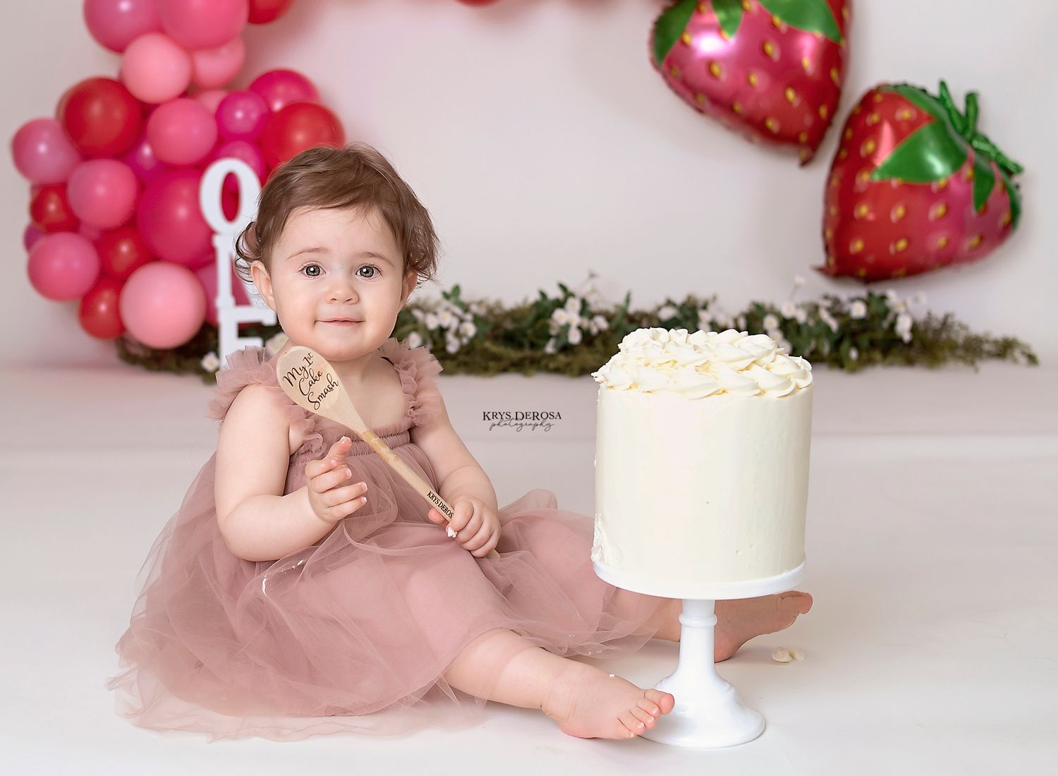 Cake smash photo with pink balloon arch and strawberry decorations.