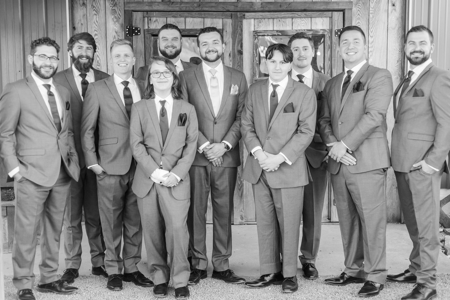A group of groomsmen in gray suits pose together in a rustic wooden venue.