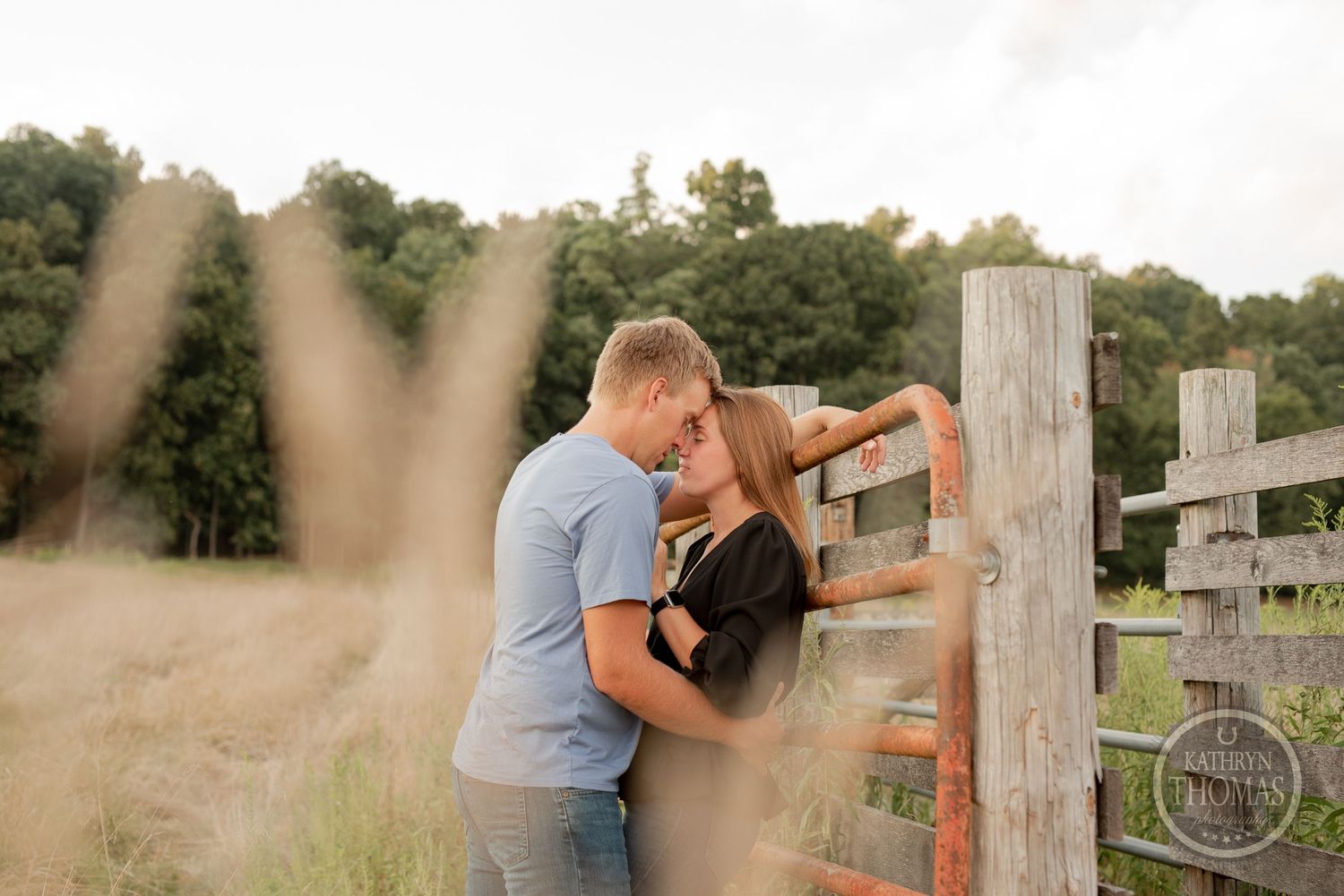 Romantic embrace by wooden fence post viewed through foreground blur.