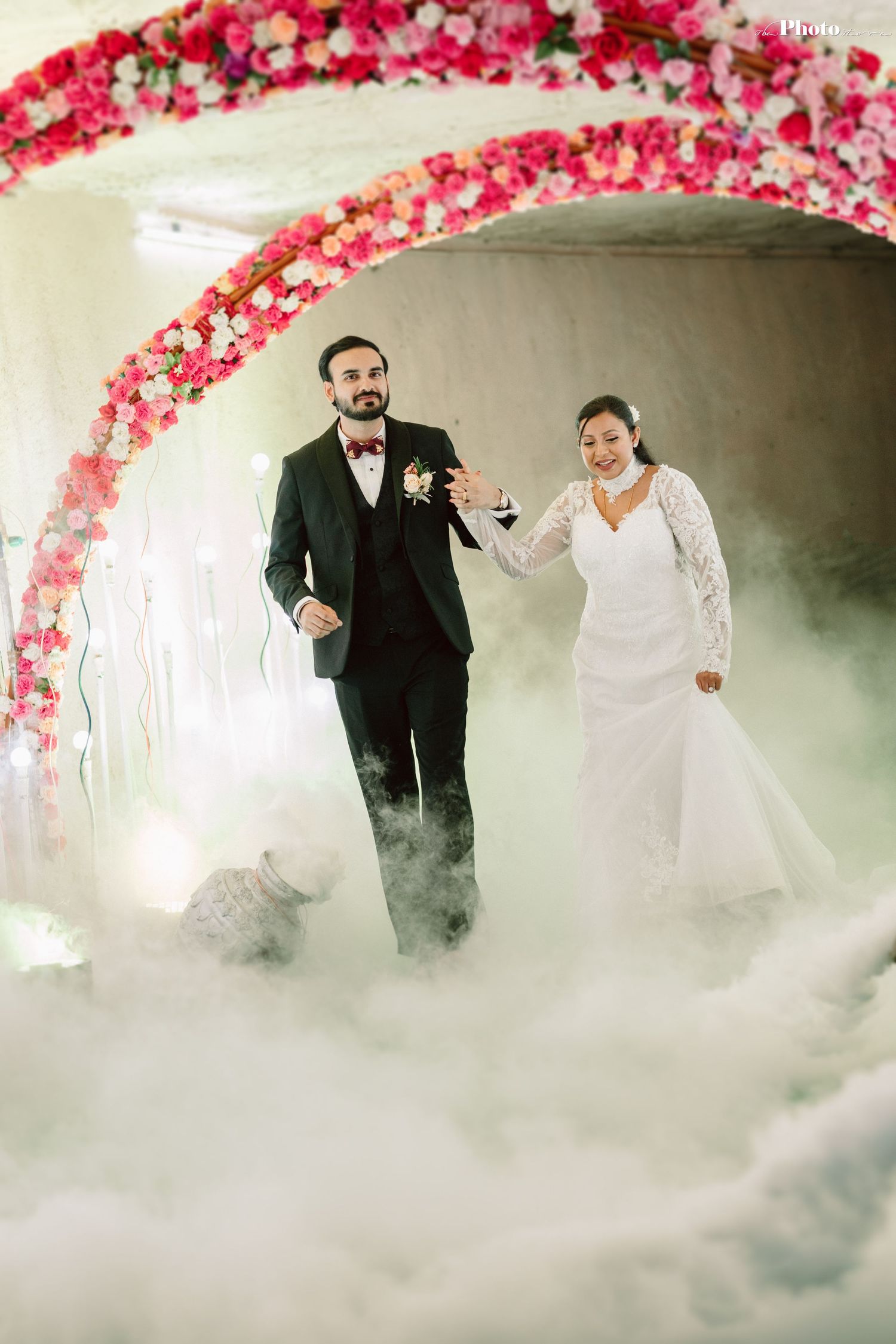 Ethereal wedding photo with couple walking through fog under pink floral arch.