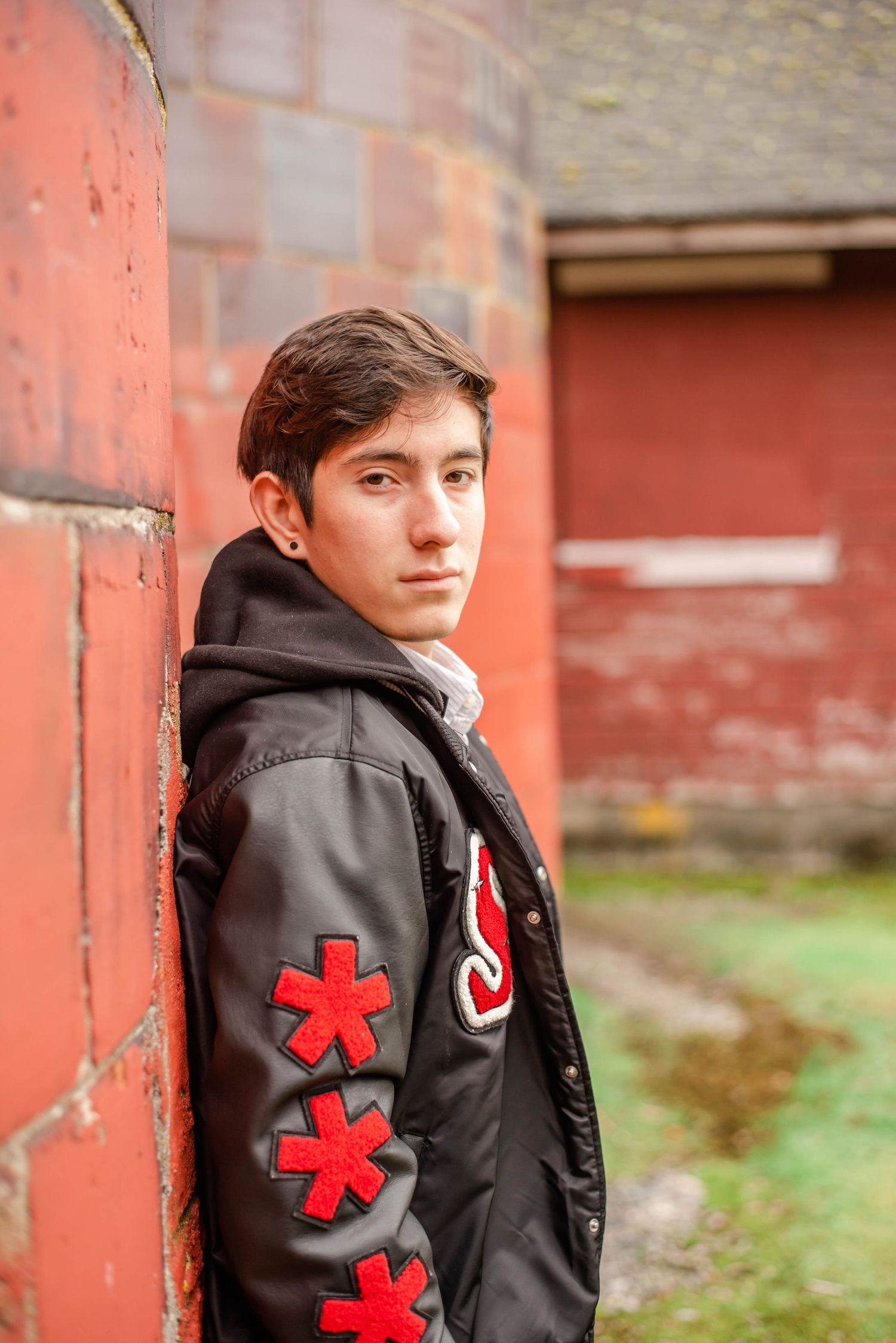 Figure in black jacket with red asterisk design poses against rustic red wall.