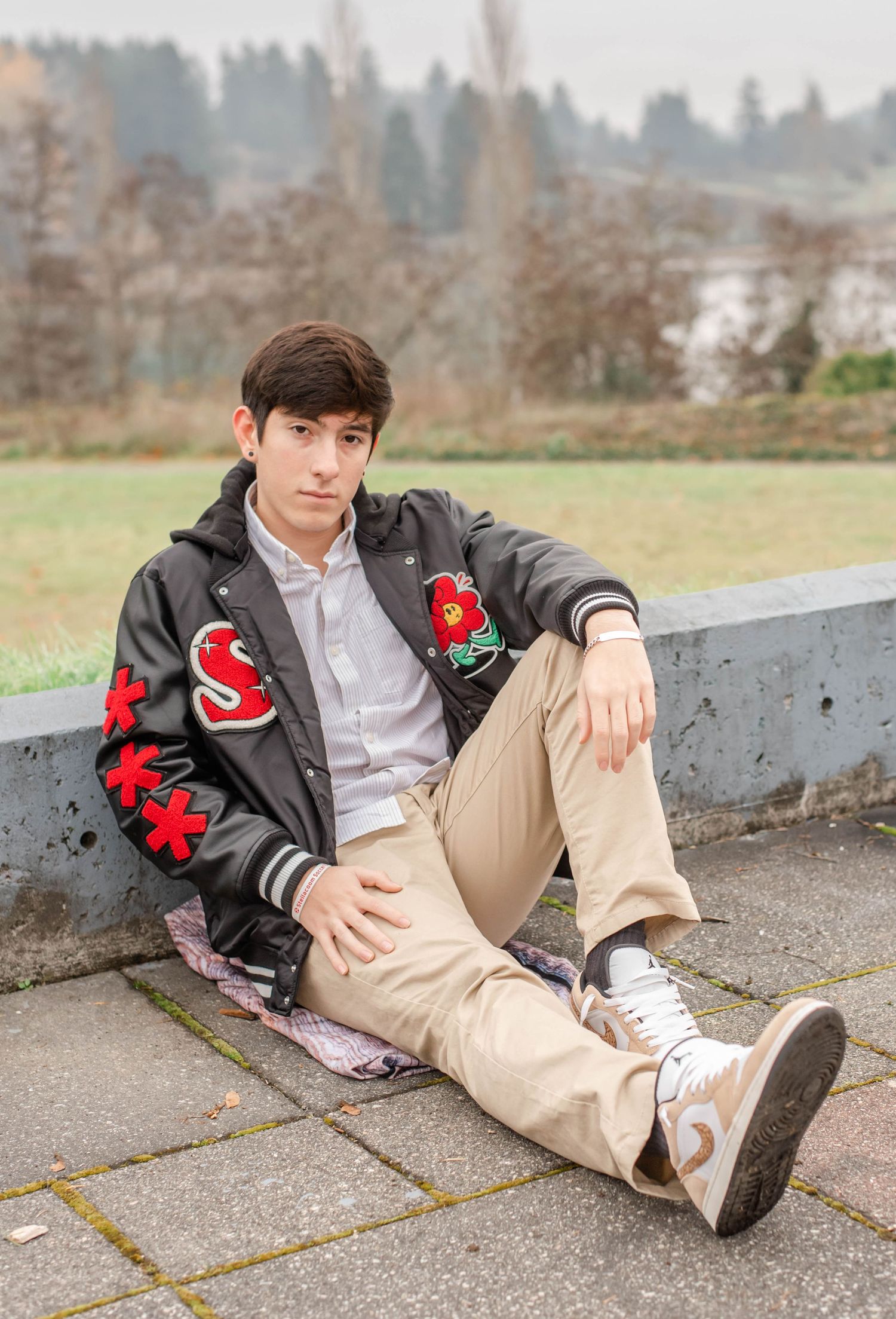 Person in black jacket with red accents relaxes on concrete ledge outdoors.