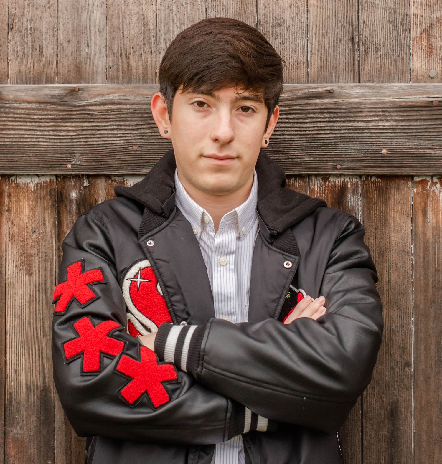 Figure wearing black jacket with red details poses against wooden wall background.