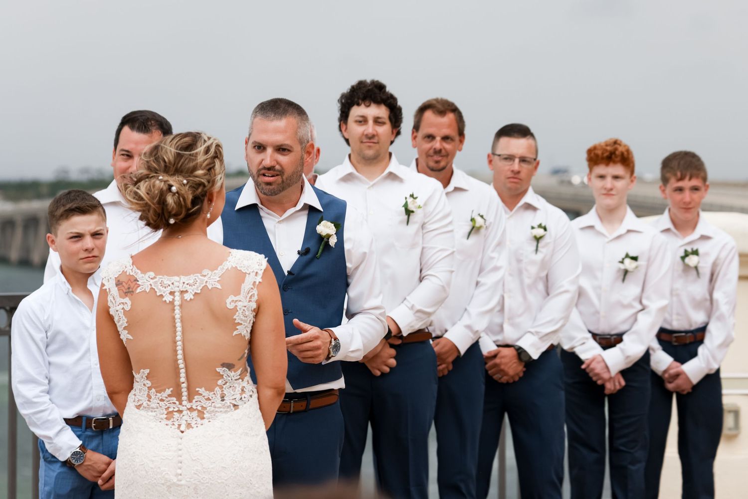 Wedding party lines up outdoors with the bride in a detailed lace back dress.