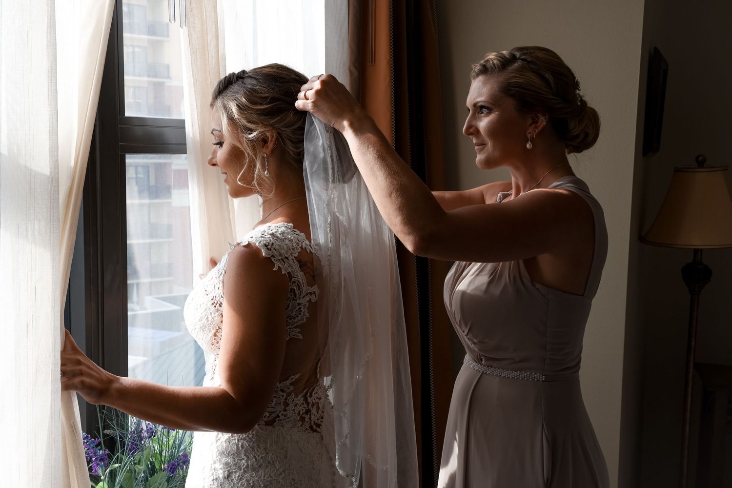 Getting ready for the wedding day as final veil adjustments are made near a window.