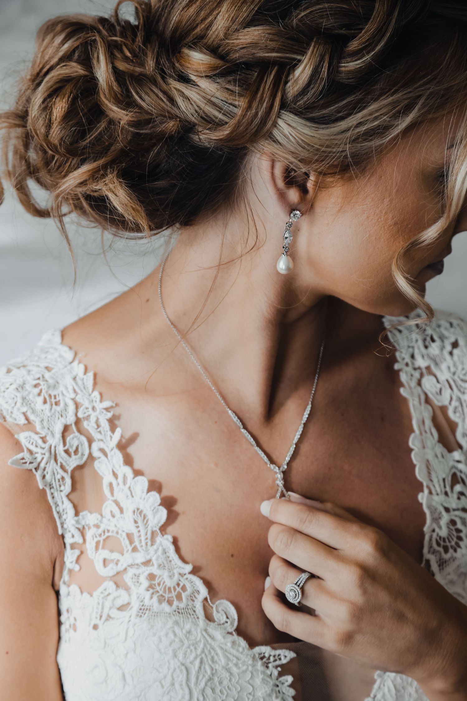 Detailed shot of bridal jewelry and lace dress with elegant updo hairstyle.