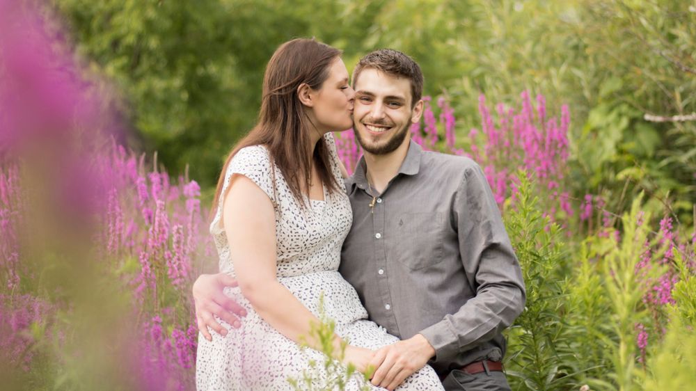 A romantic couple shares a tender moment among pink wildflowers in a garden setting.