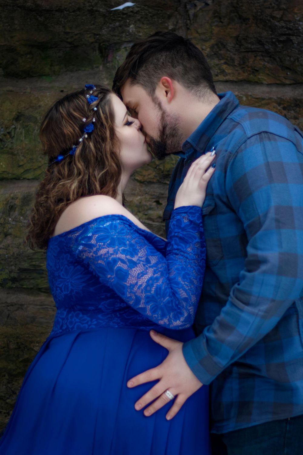 Romantic couple's photoshoot featuring blue lace dress and plaid shirt against stone wall.