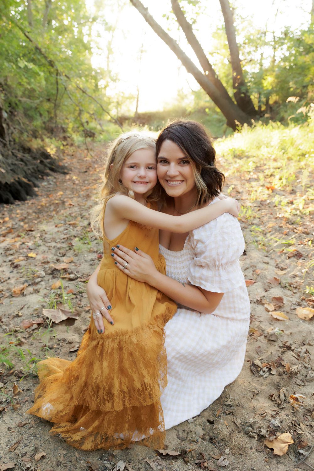 A warm embrace shared between two people wearing a mustard dress and white dress on a forest trail.