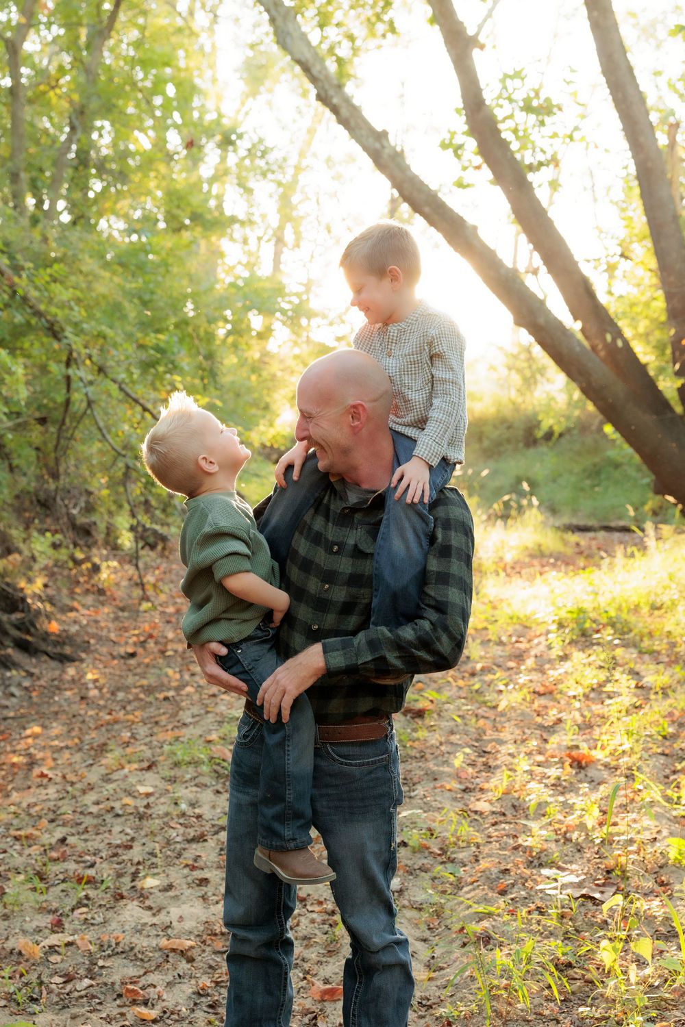 Playful family moment captured on a forest path with warm sunlight filtering through trees.