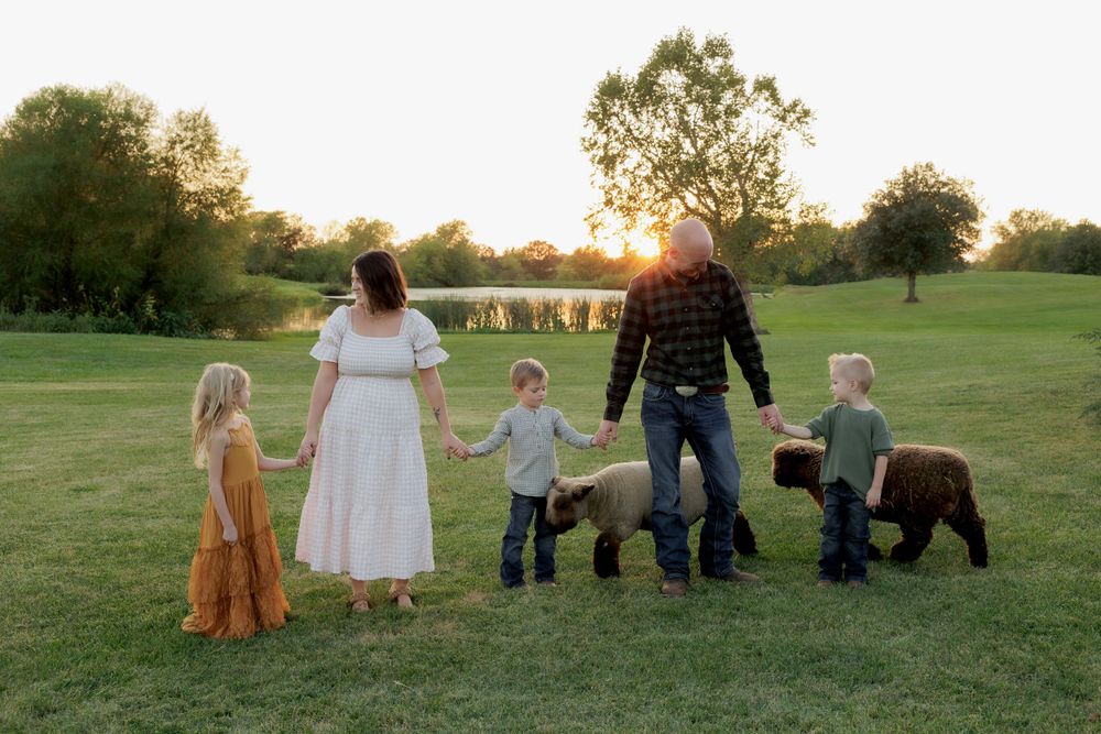 A family walks together at sunset in a grassy field with their dog.