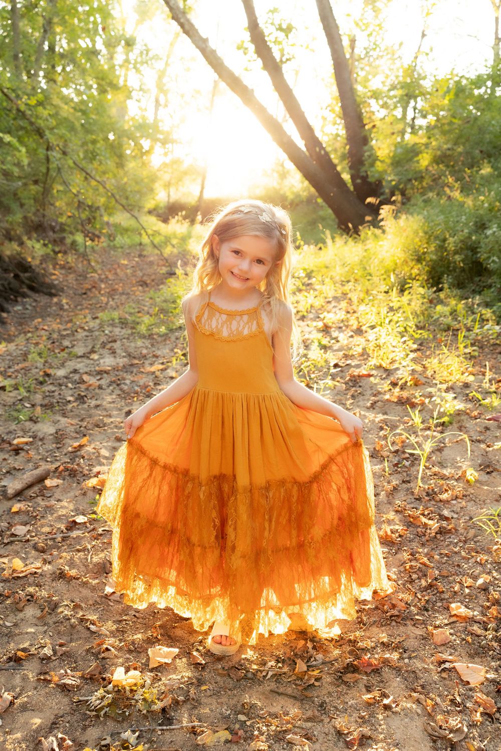 Young person twirls in a flowing mustard-colored dress on an autumn forest path.