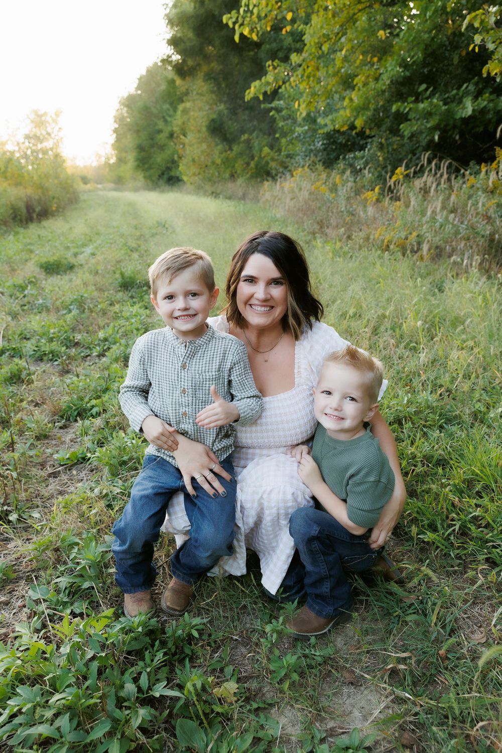 A family portrait taken outdoors in a lush green setting during golden hour.