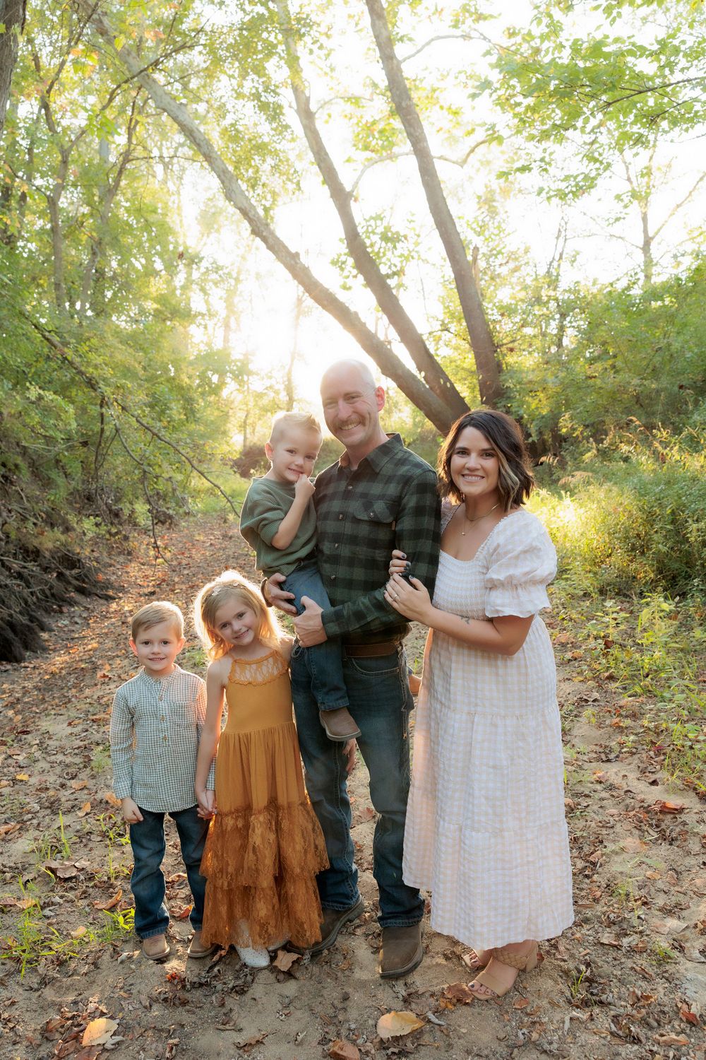 A family of five poses together on a wooded trail during golden hour.