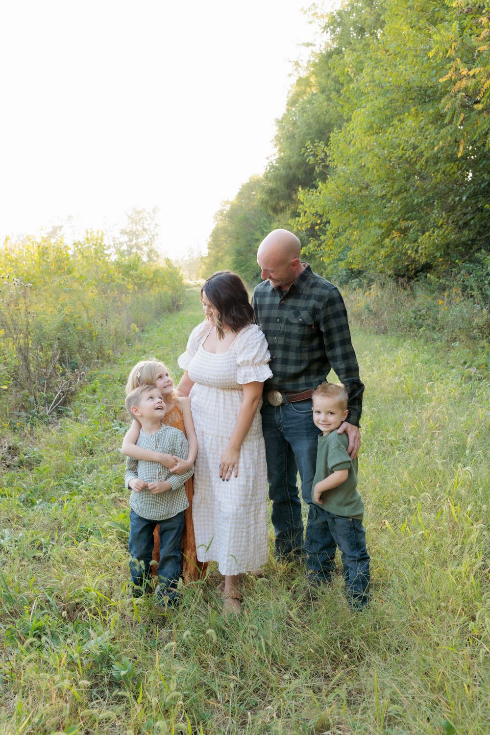 Family of four poses together in tall grass during sunset photo session.