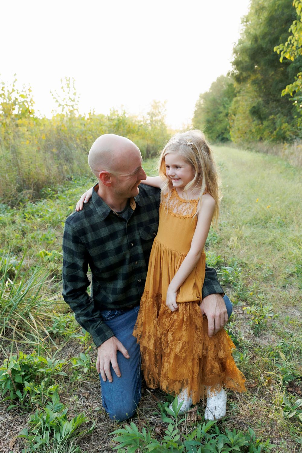 Two people share a tender moment on a grassy trail during golden hour.