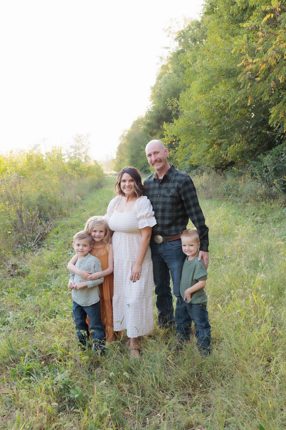 Candid family portrait in natural setting with golden sunlight filtering through trees.
