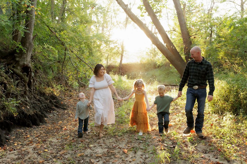 Family walking hand in hand down a sunlit forest path during autumn.
