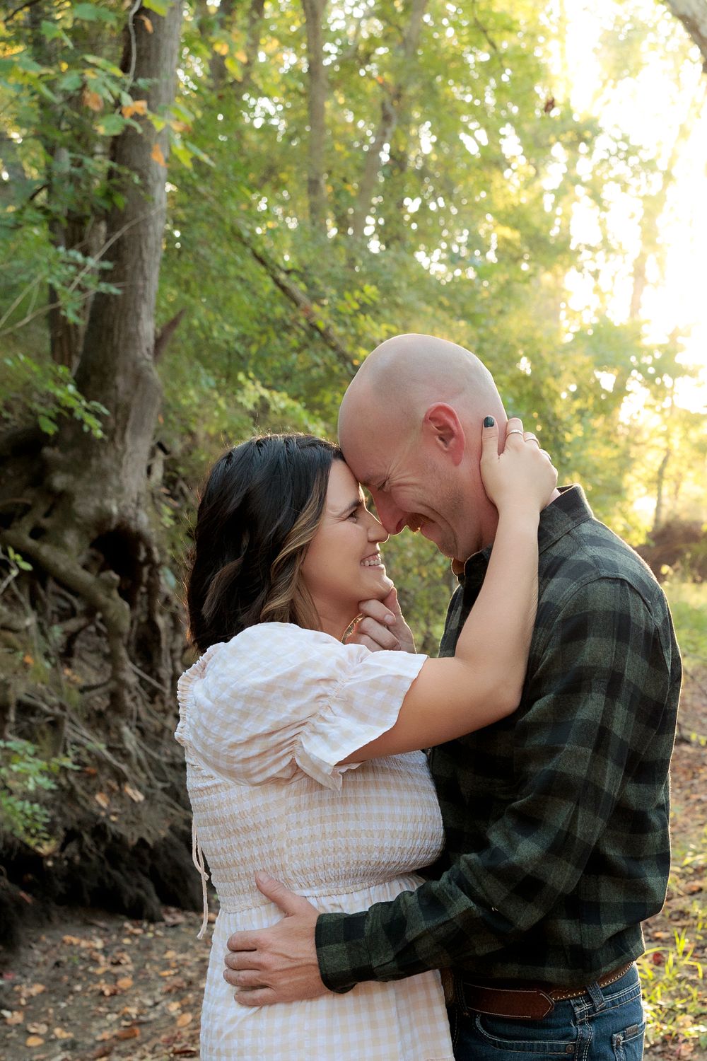 Intimate couple portrait embracing in wooded setting with dramatic sunlight.