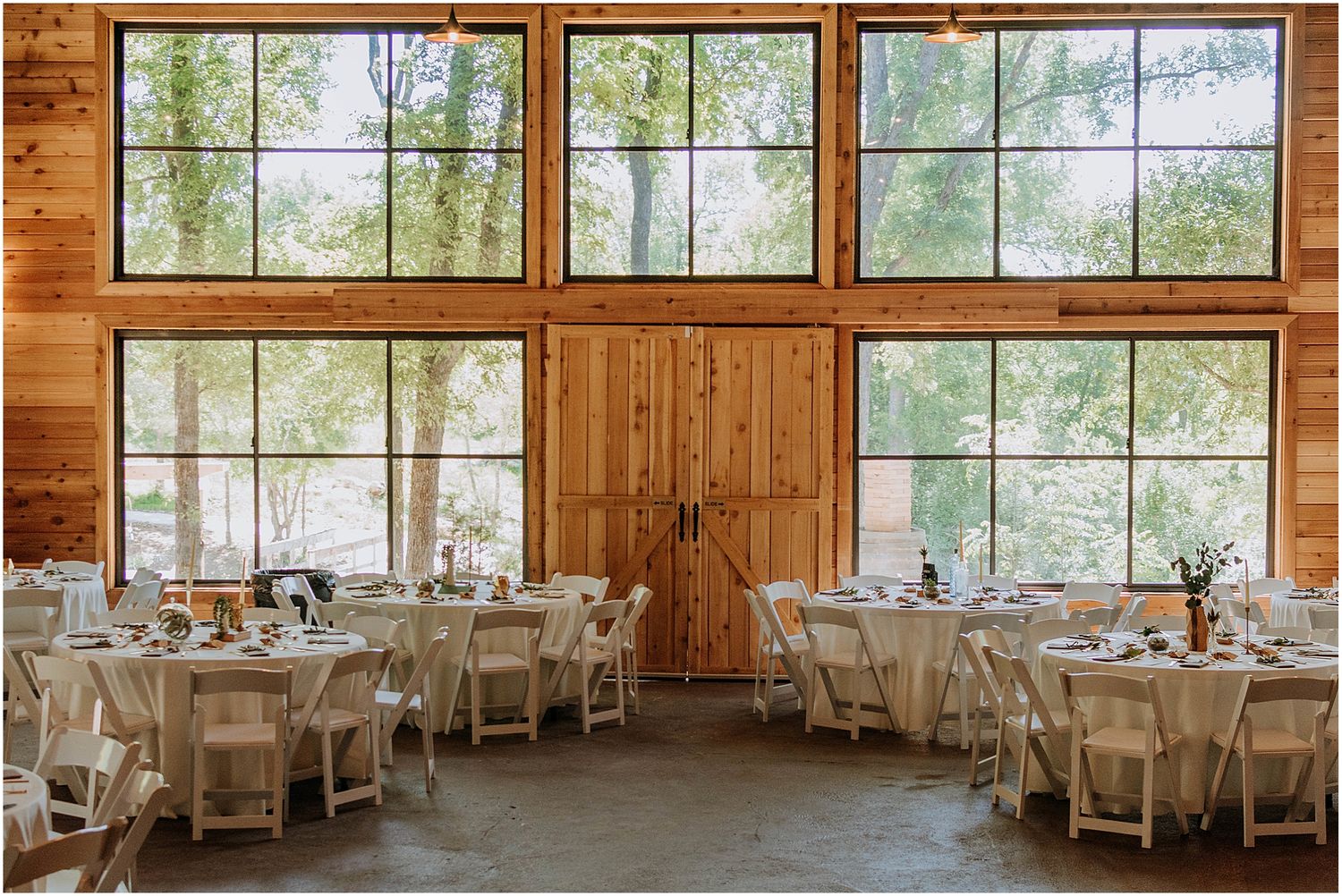 Rustic wedding reception venue with large windows and white table settings.