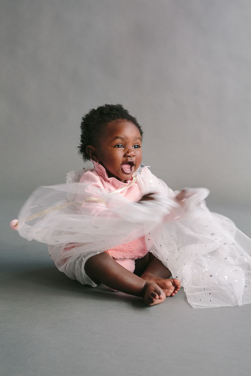 a child on a pink dress plays on a grey backdrop during a studio session by NYC Family Photographer Paula Ortiz
