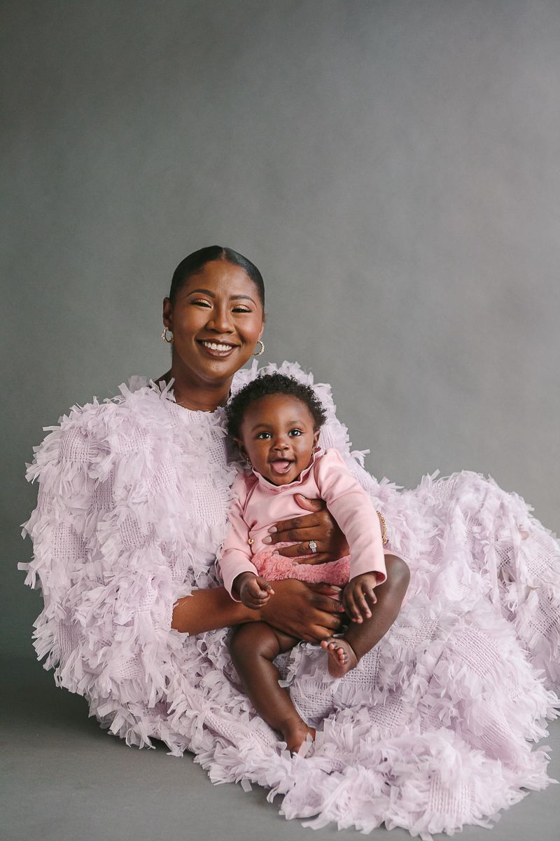 a mother and child sit on a grey backdrop wearing purple and pink dresses by NYC Family Photographer Paula Ortiz