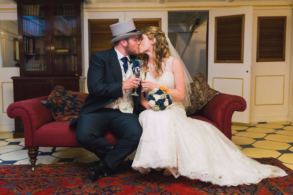 A bride and groom toast and share a kiss on a red sofa in an ornate room aboard HMS Warrior, Portsmouth.