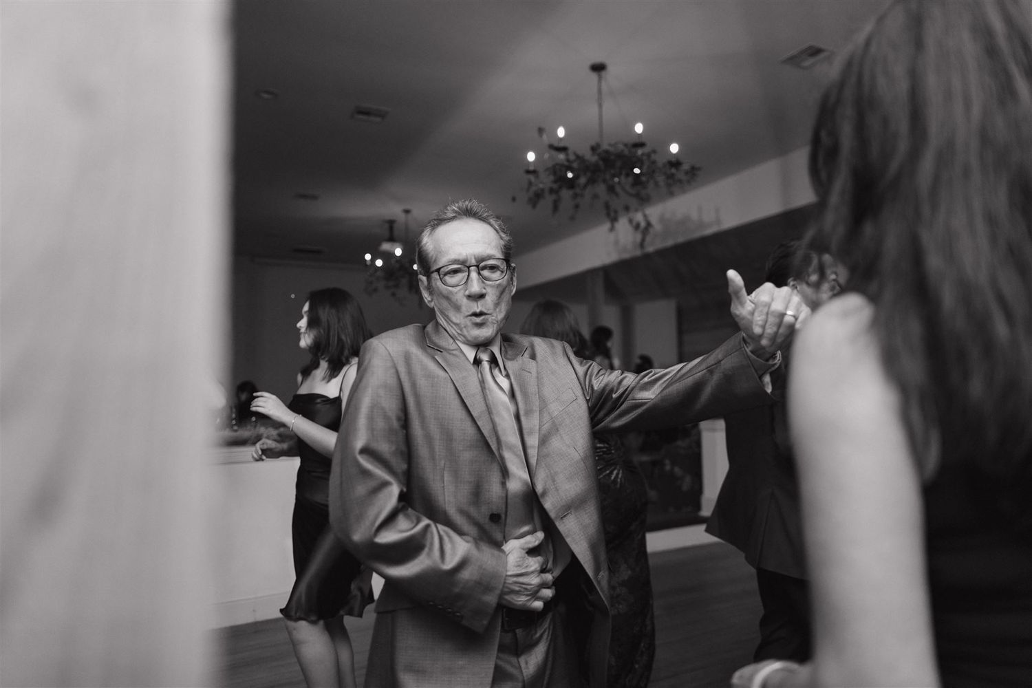 A candid black and white photo of guests dancing at an indoor celebration.