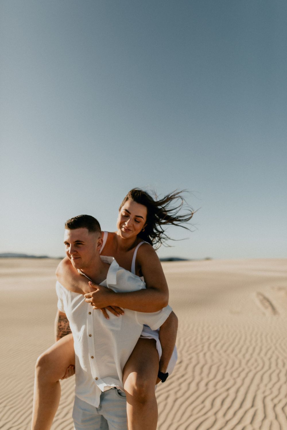 Playful couple having fun on sand dunes during a sunny desert photoshoot.