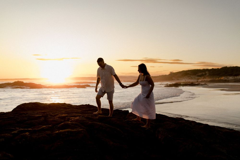 Silhouette of couple walking along rocky coastline during golden sunset.