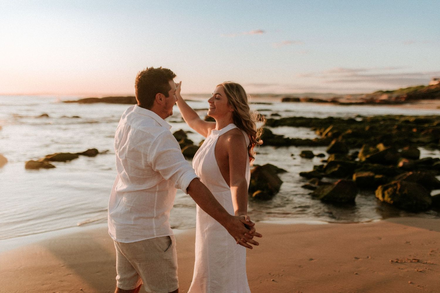 A romantic sunset beach photo with rocky coastline and ocean waves.