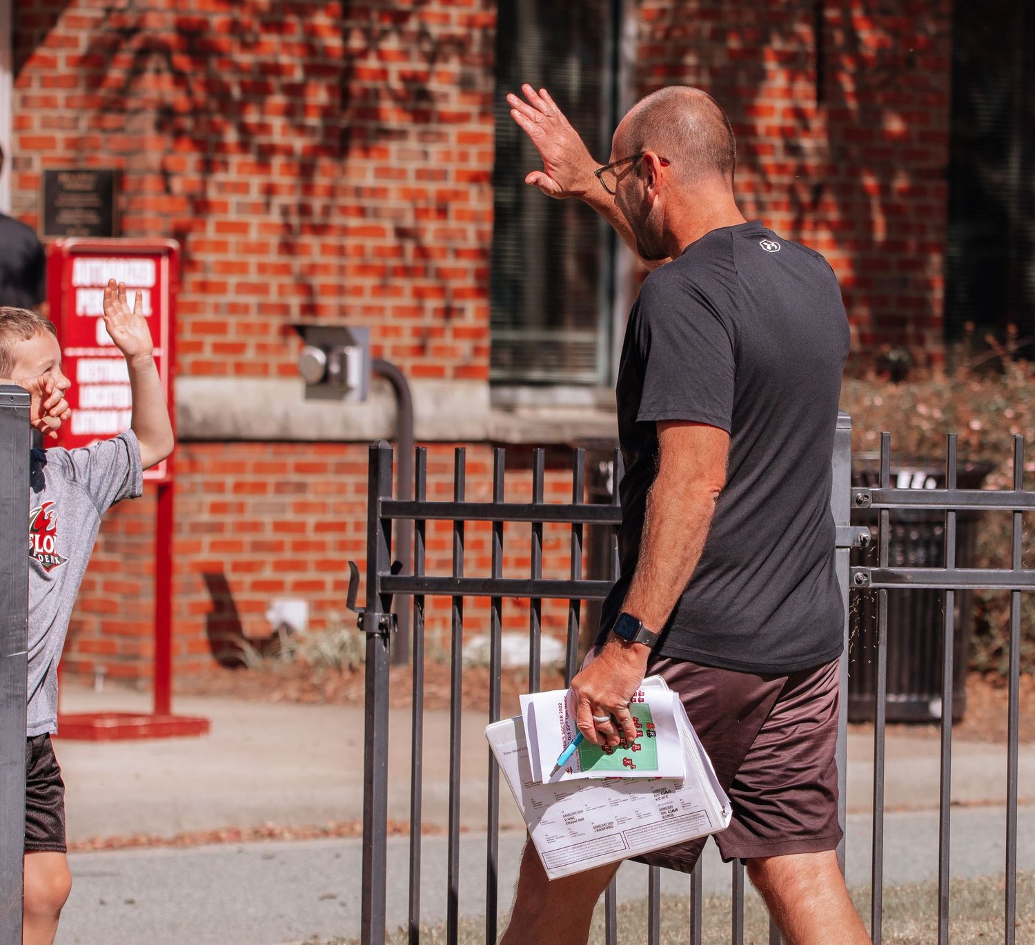 Person gestures while holding newspaper outside brick building with iron fence.