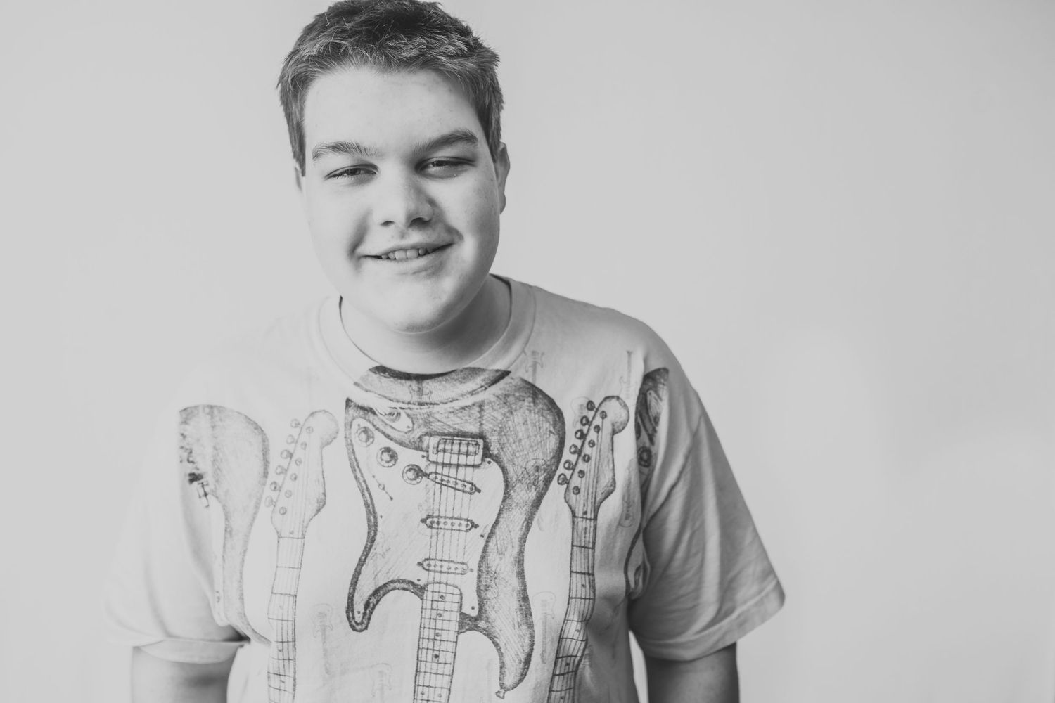 Black and white portrait of someone smiling while wearing a t-shirt with guitar designs.