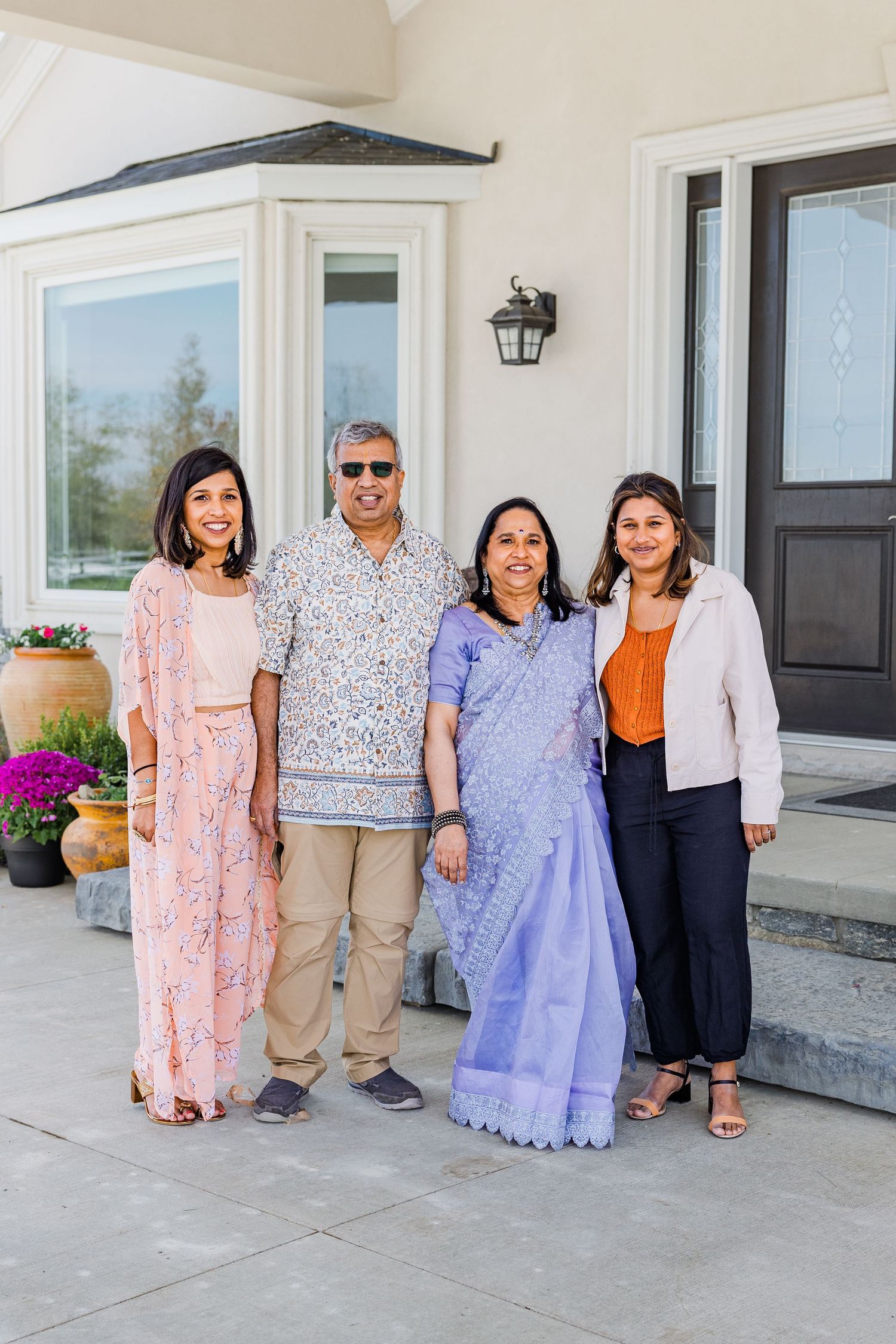 Family photo showing traditional and modern outfits including a blue sari and pink floral dress on front porch.