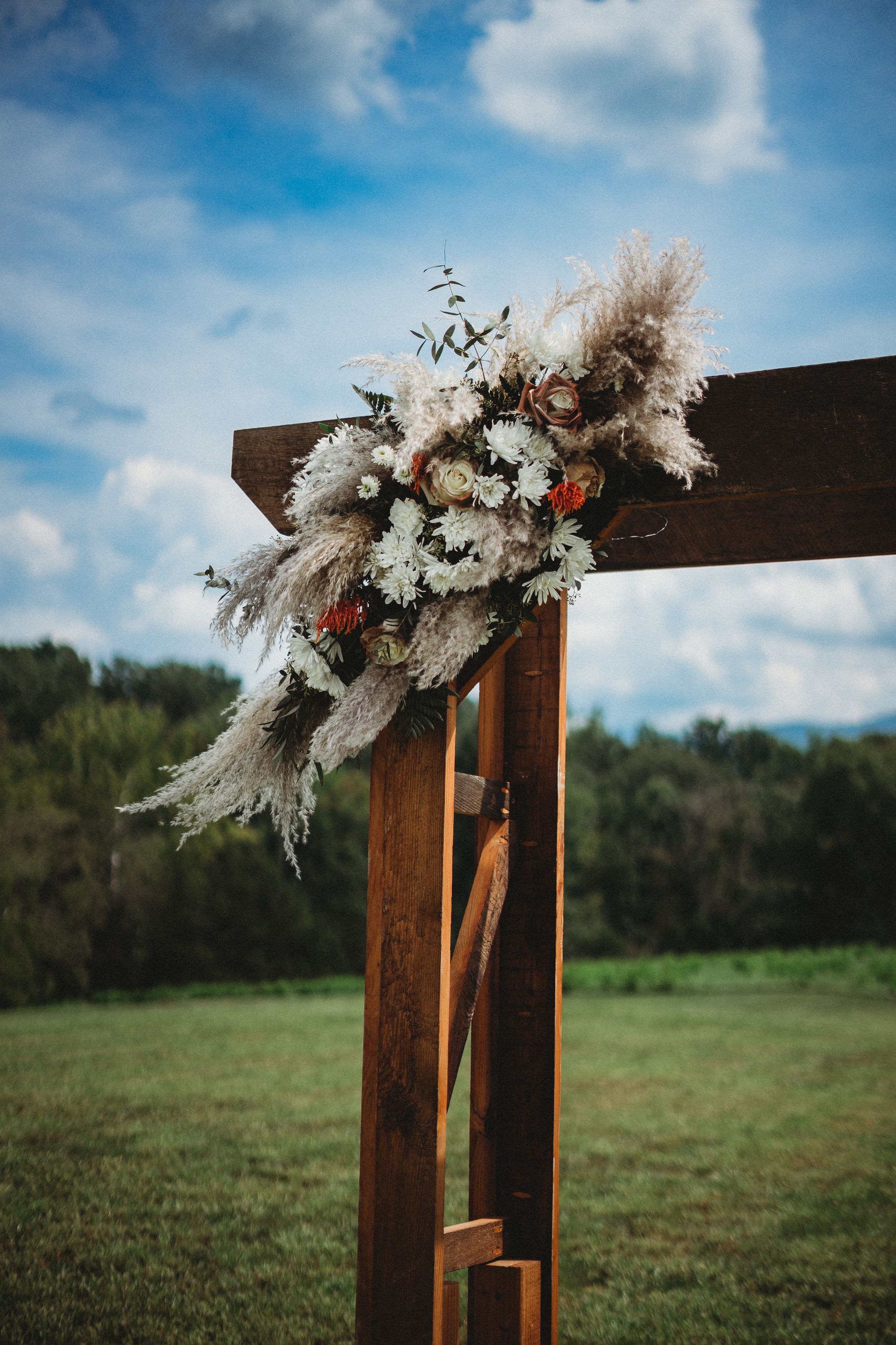 Wooden wedding arch decorated with white flowers and pampas grass against a blue sky.
