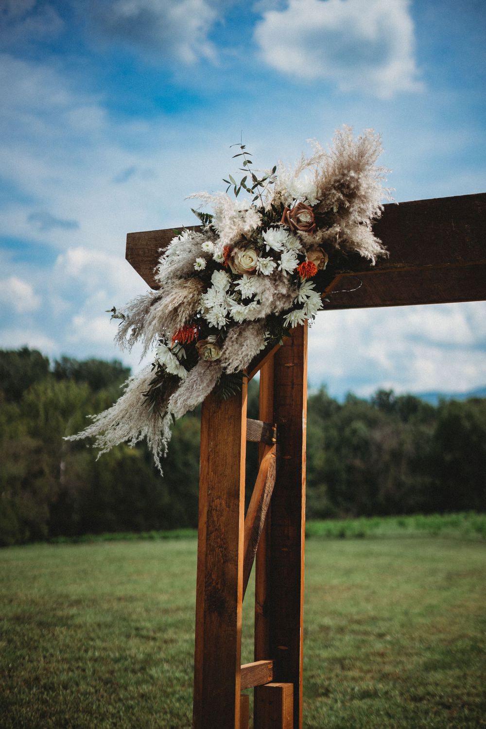 Wooden wedding arch decorated with white flowers and pampas grass against a blue sky.