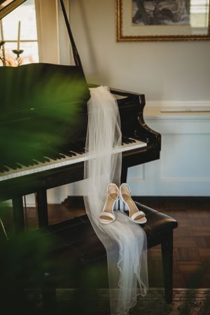 Wedding dress and shoes displayed near black grand piano in elegant room.