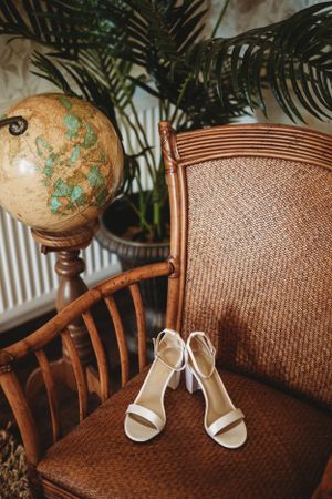 White bridal shoes displayed on a wicker chair with decorative globe accent.
