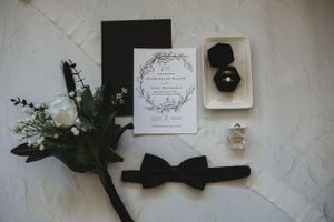 Minimalist wedding styling with black bow tie and floral arrangements on white surface.