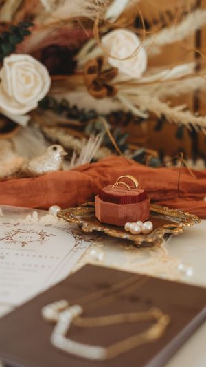 Wedding rings and pearls displayed on rustic brown fabric with delicate details.