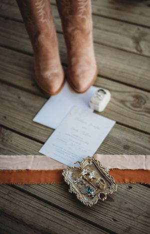Vintage brooch and wedding stationery with cowboy boots on wooden deck.