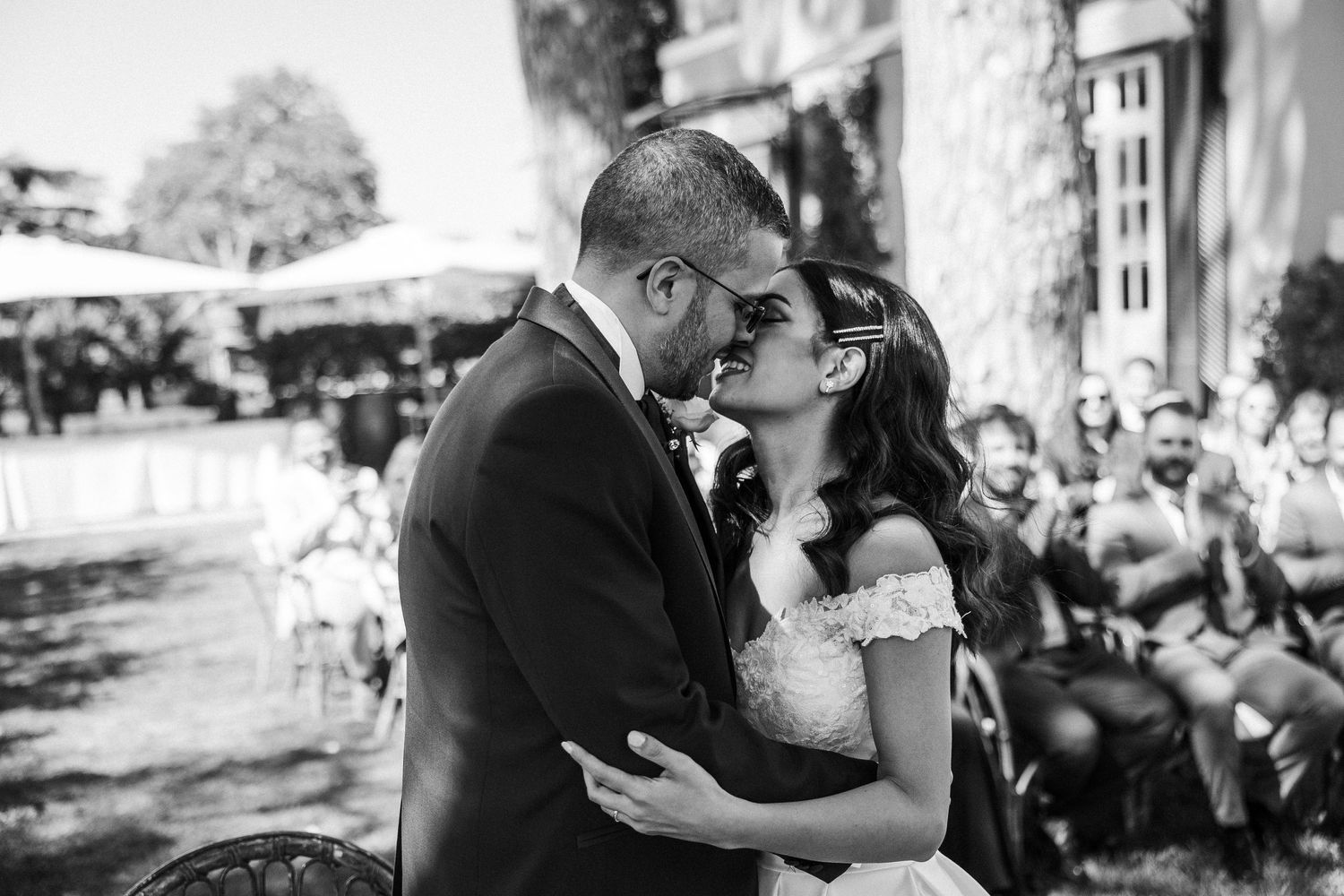 A romantic black and white moment captured between newlyweds sharing an intimate kiss outdoors.