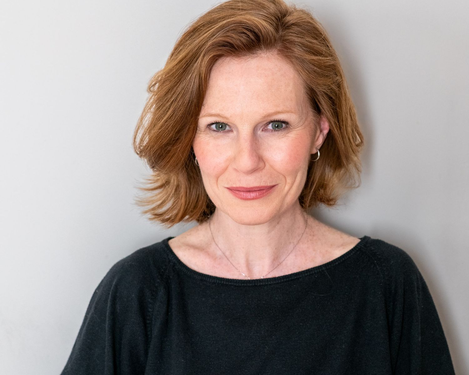 a middle aged woman with red hair and fair skin in front of a white wall